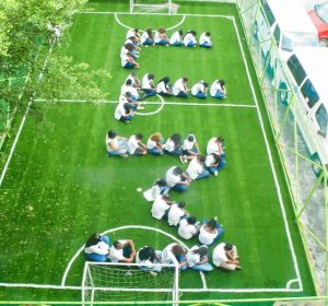 LLM staff seated on a football pitch to form the letter LLM.